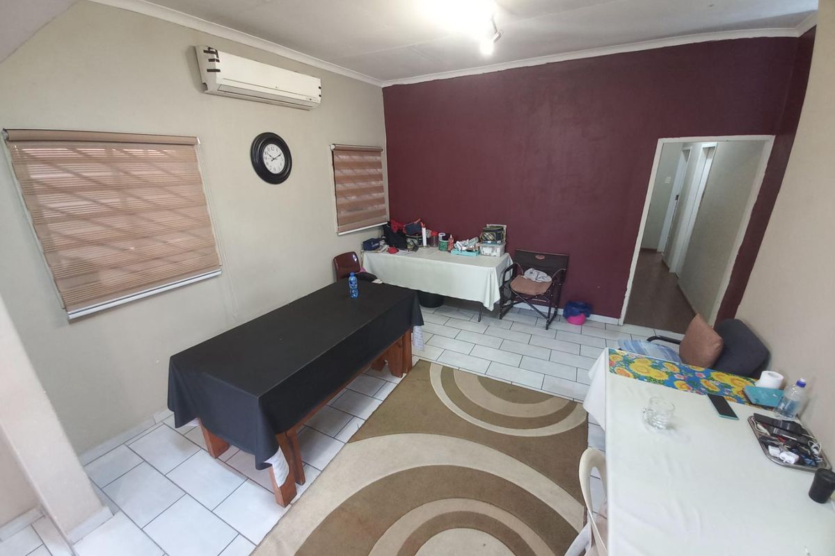 A functional living area featuring tiled flooring, a wall-mounted air conditioning unit, and dual-tone wall finishes with access to an adjacent hallway.