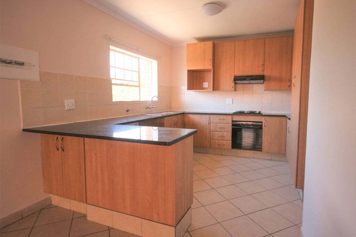 A functional kitchen featuring laminate cabinetry, dark granite countertops, built-in oven, gas hob, and tiled flooring in a clean, empty space.