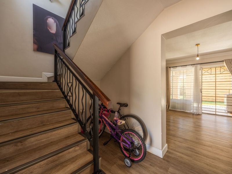 A bright hallway featuring a staircase with a wrought iron balustrade and wooden handrail, leading into an adjacent living area with sliding door access.