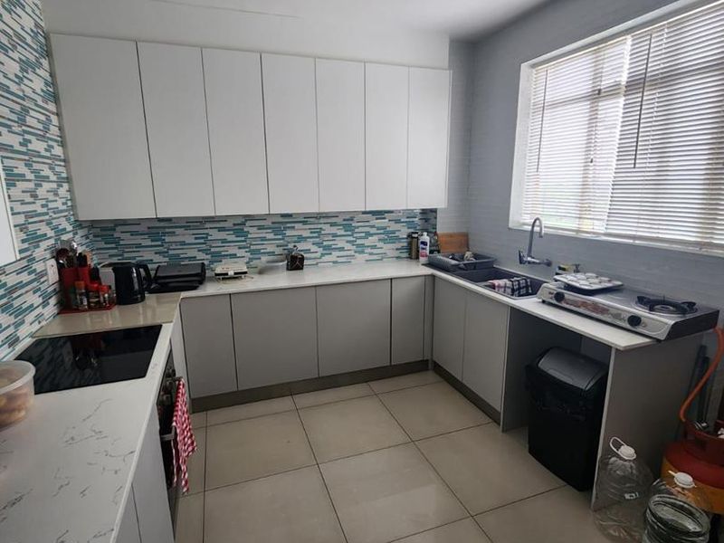 Modern kitchen featuring white and grey cabinetry, stone countertops, a mosaic tile backsplash, and large format floor tiles with ample natural light.