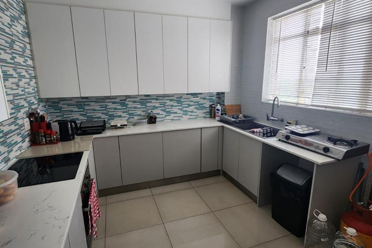 Modern kitchen featuring white and grey cabinetry, stone countertops, a mosaic tile backsplash, and large format floor tiles with ample natural light.