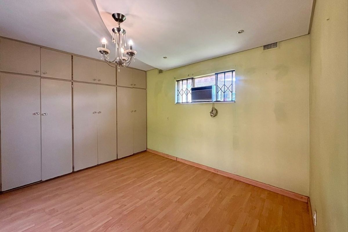 A spacious bedroom featuring built-in cupboards, laminate flooring, and an integrated air conditioning unit, offering a blank canvas for personalization.