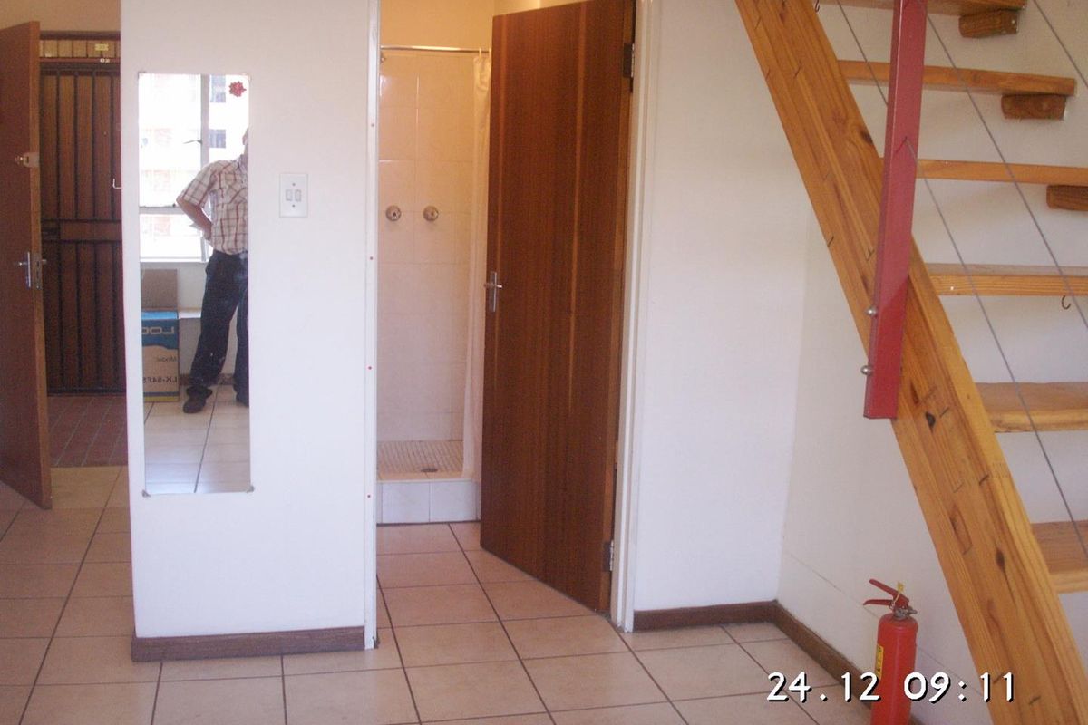 A functional hallway area featuring tiled flooring, a timber staircase, and direct access to a shower room.