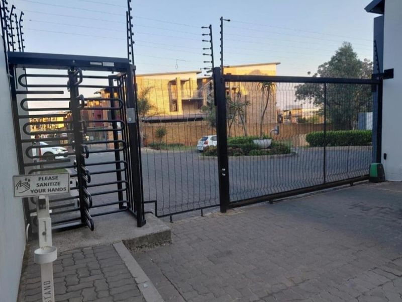 Secure apartment complex entrance featuring a sliding gate, pedestrian turnstile, and perimeter electric fencing.