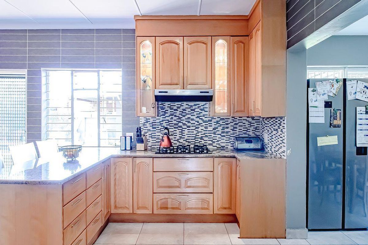 A functional kitchen featuring wooden cabinetry, granite countertops, a gas hob with an extractor fan, and tiled splashbacks.
