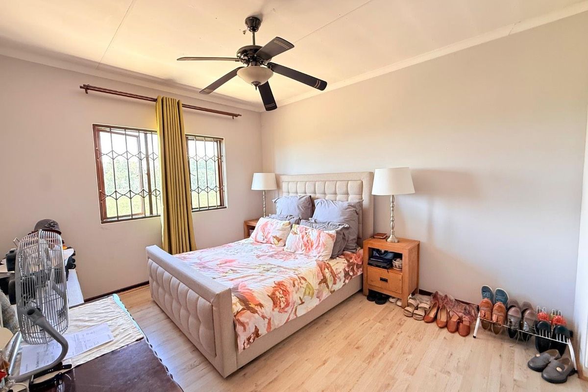 A well-lit bedroom featuring light wood-look flooring, a ceiling fan, and security bars on the windows.