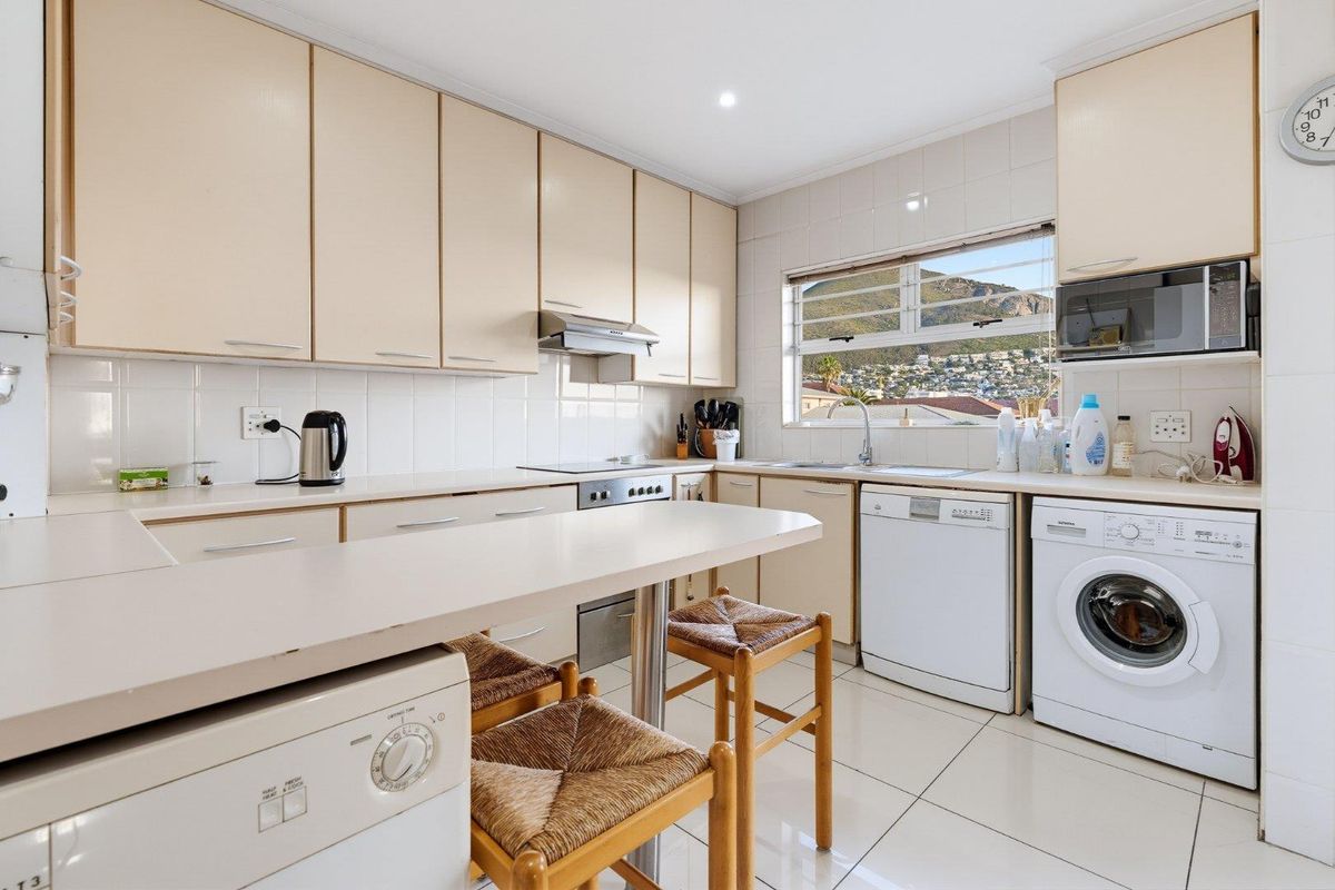 Functional kitchen featuring light-toned cabinetry, tiled backsplash, breakfast bar, and integrated laundry and dishwasher appliances with mountain views.