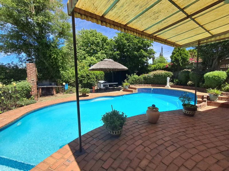 Outdoor pool area featuring a swimming pool, brick paved patio, and a built-in braai, set within a landscaped garden.