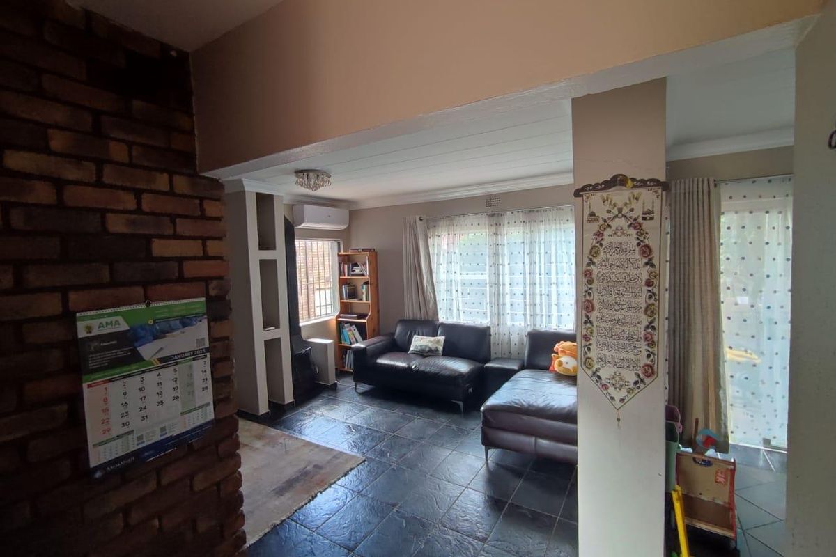 A living room featuring a rustic exposed brick feature wall, dark tiled flooring, and a wall-mounted air conditioning unit.