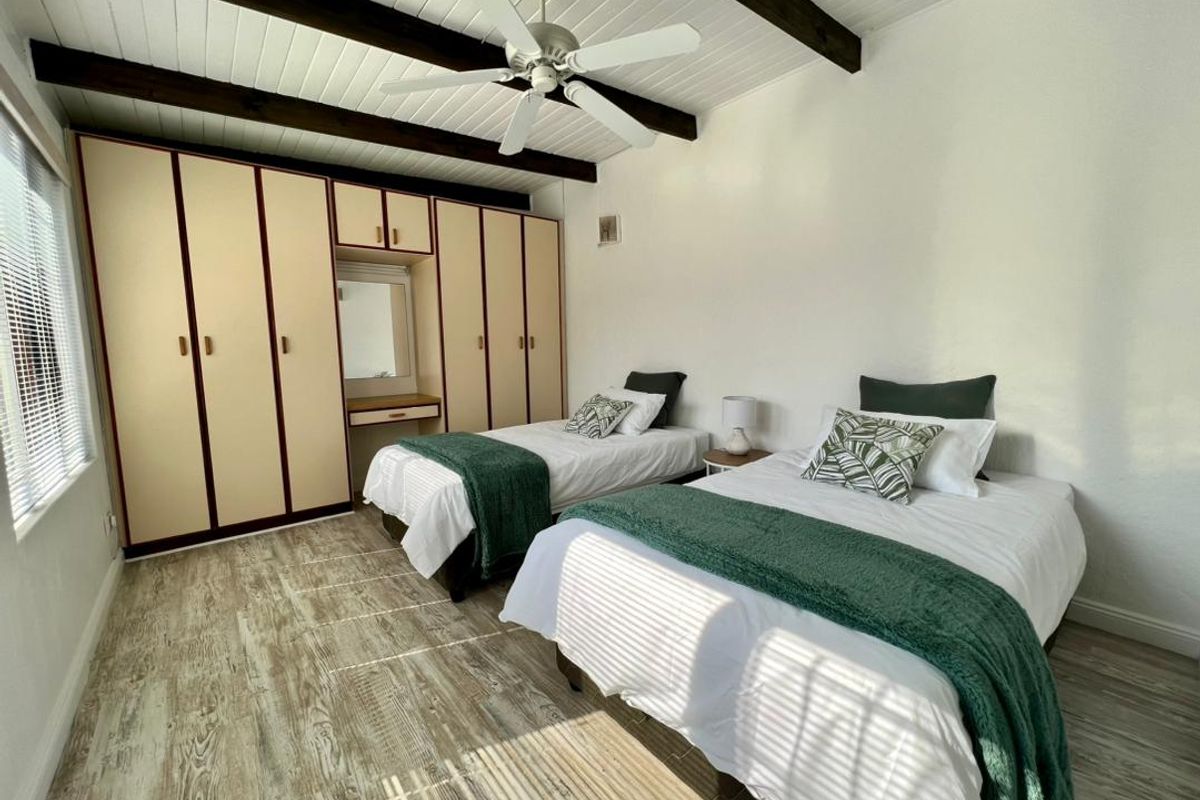 A bedroom featuring built-in cupboards, exposed timber ceiling beams, a ceiling fan, and laminate flooring.