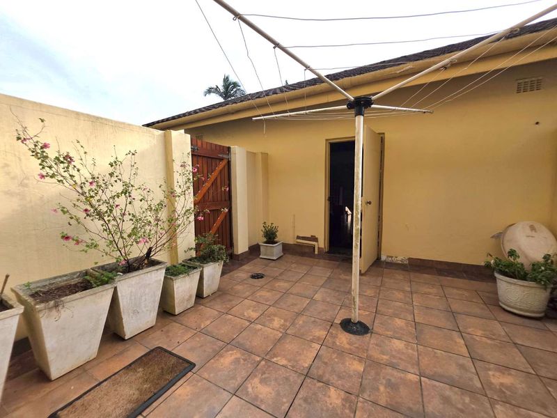 A private rear courtyard featuring tiled flooring, a boundary wall with a wooden gate, and a fixed rotary clothesline.