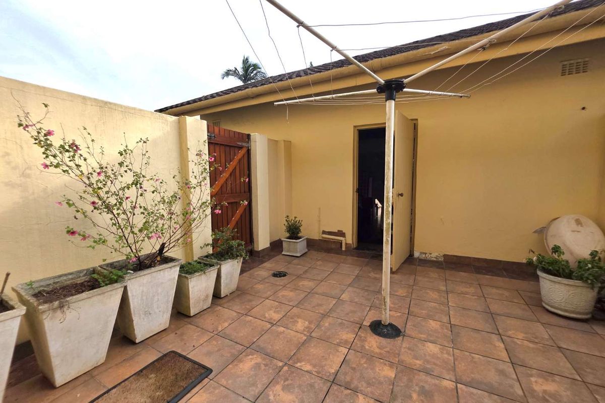 A private rear courtyard featuring tiled flooring, a boundary wall with a wooden gate, and a fixed rotary clothesline.