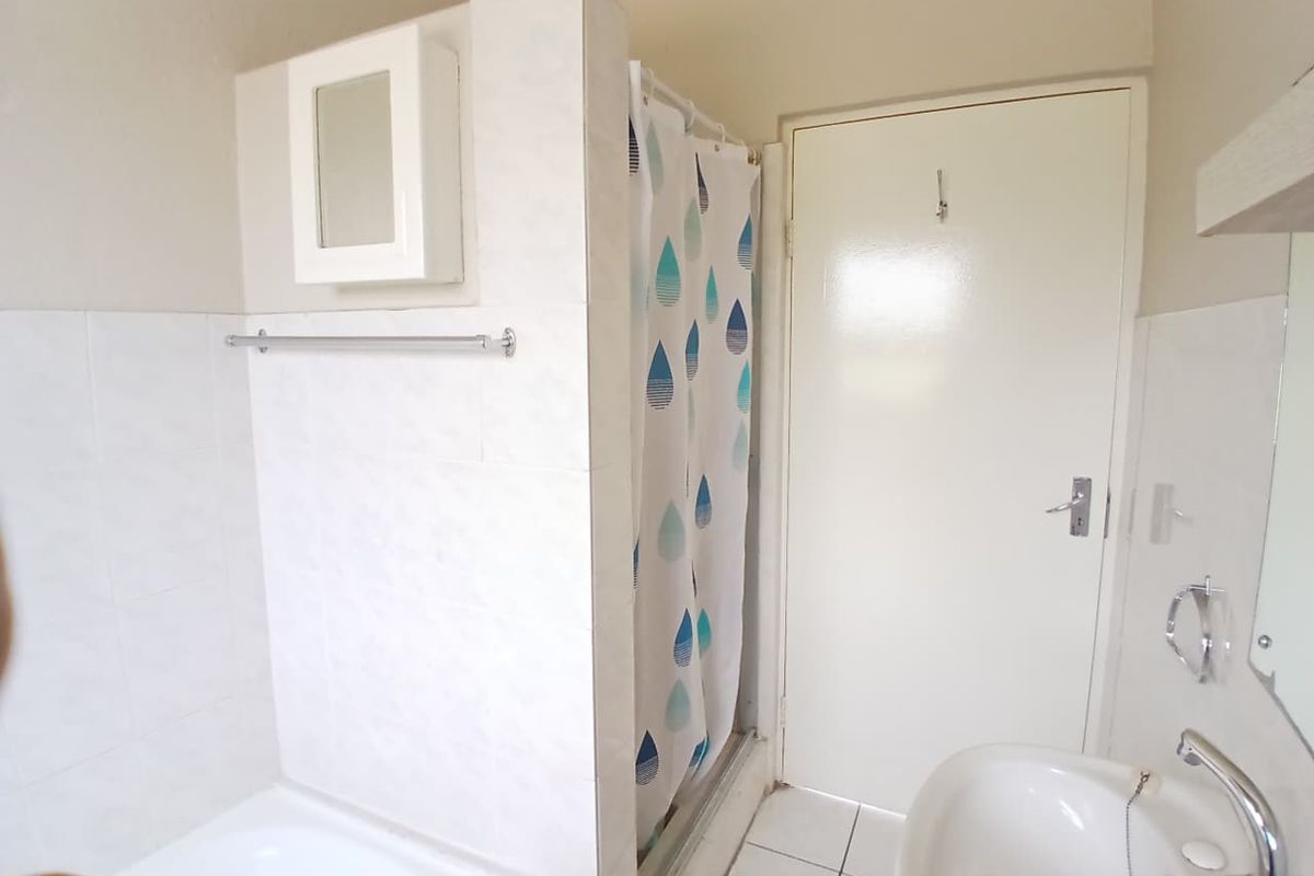 A functional bathroom featuring a shower enclosure, tiled walls, and a pedestal basin, offering a clean and practical layout.
