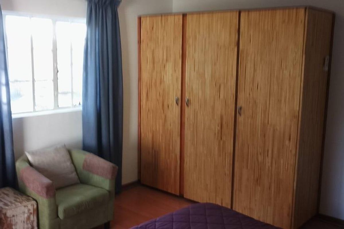 A bedroom featuring a large built-in wooden wardrobe and a window with curtains.