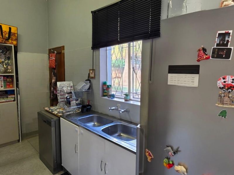 A functional scullery area featuring a double basin sink, built-in cabinetry, and a window with security bars.