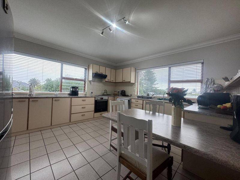 Functional kitchen featuring ample built-in cabinetry, laminate countertops, integrated oven, extractor fan, and ceramic tile flooring with large windows providing natural light.