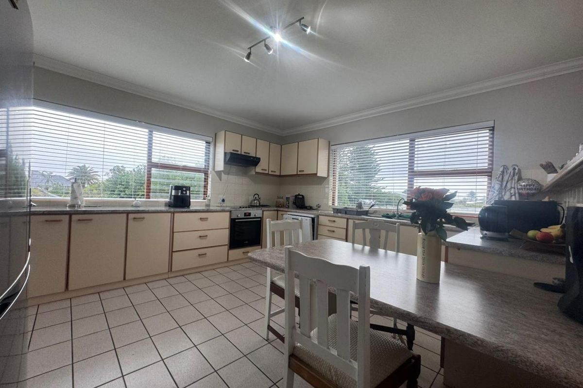 Functional kitchen featuring ample built-in cabinetry, laminate countertops, integrated oven, extractor fan, and ceramic tile flooring with large windows providing natural light.
