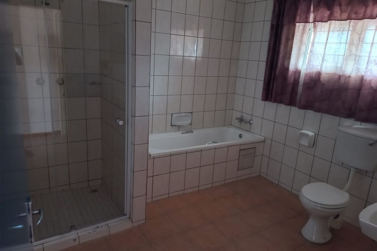 A dated bathroom featuring a built-in bathtub, separate shower enclosure, and toilet with full-height wall tiling and floor tiles.