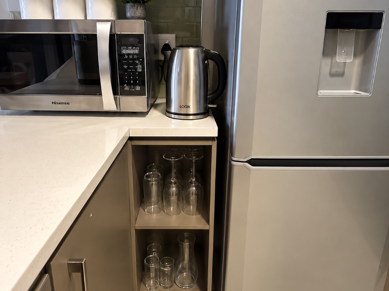 A modern kitchen corner featuring stone countertops, subway tile backsplash, built-in microwave, and integrated open shelving for glassware storage.