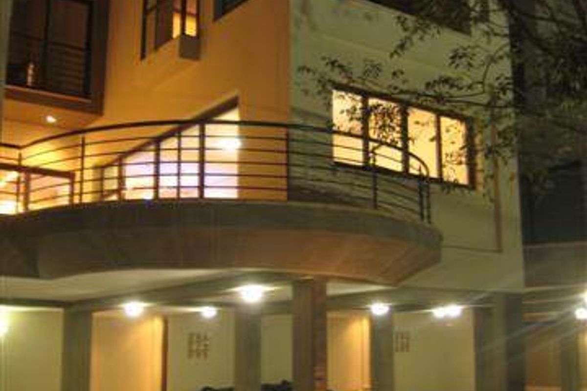 Rear view of a multi-story townhouse featuring a curved balcony, paved under-cover parking area, and modern architectural lighting.