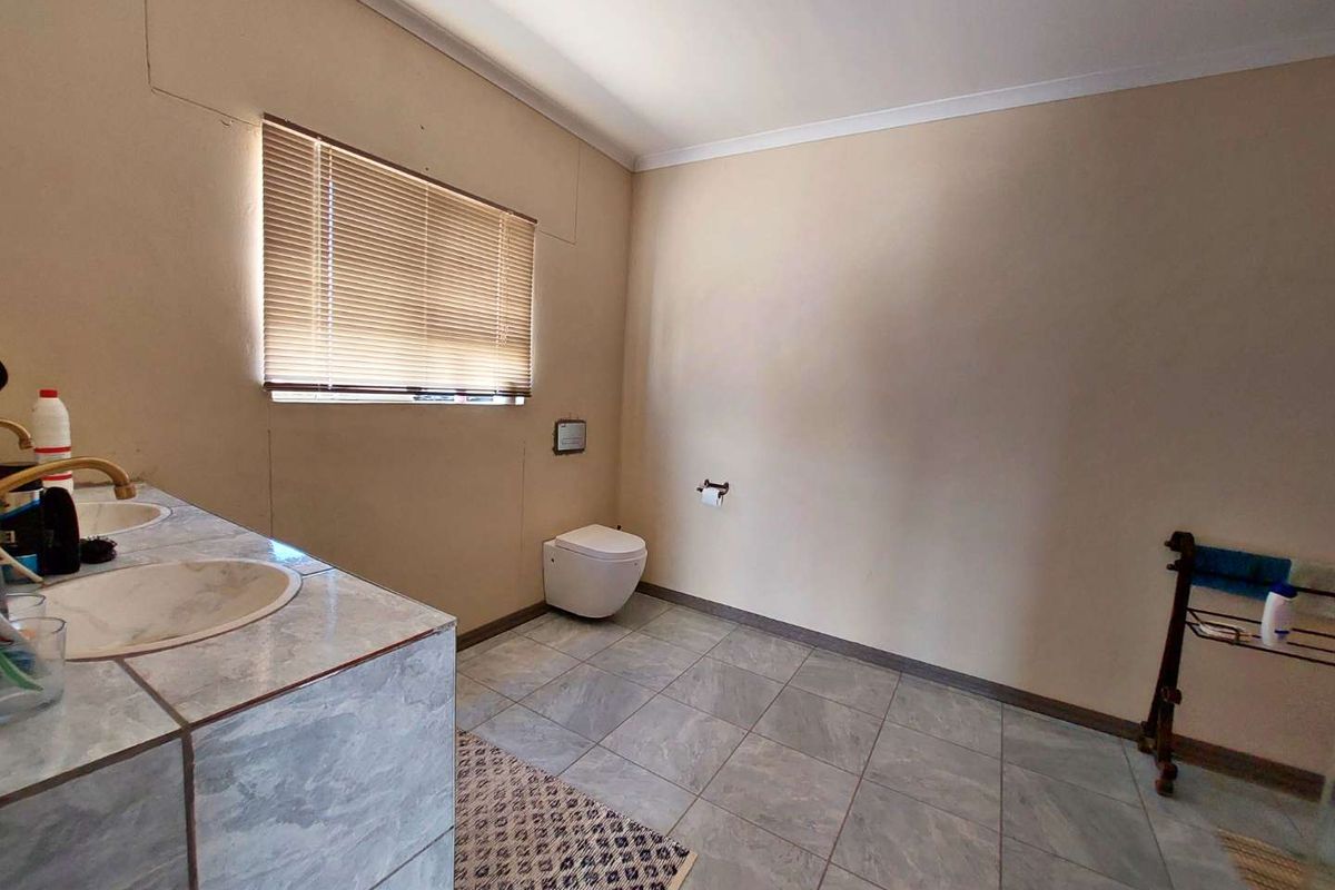 A functional bathroom featuring a tiled vanity with dual basins, a wall-mounted toilet, and tiled flooring.