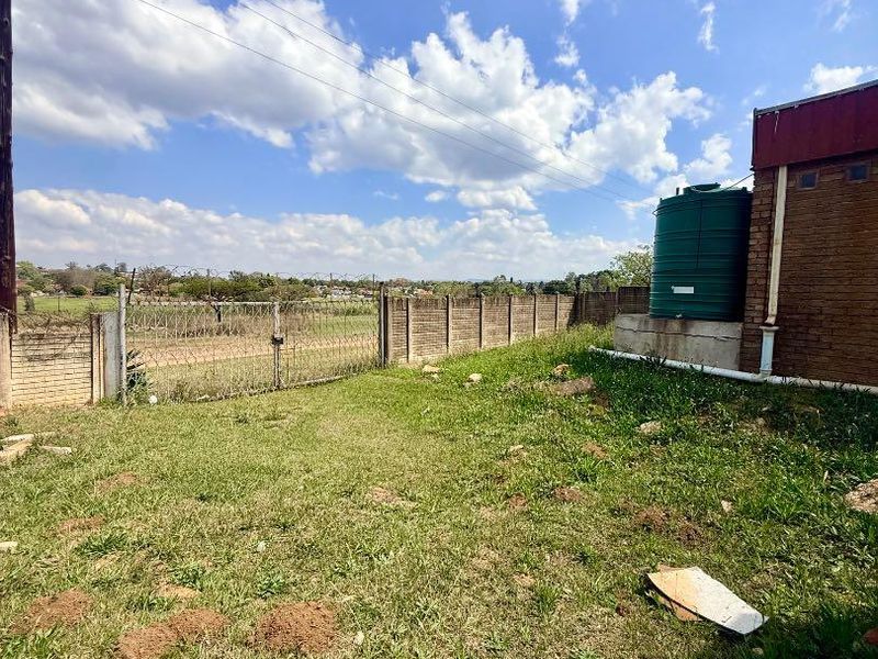 Rear exterior area featuring a brick boundary wall with razor wire fencing and a green water storage tank.