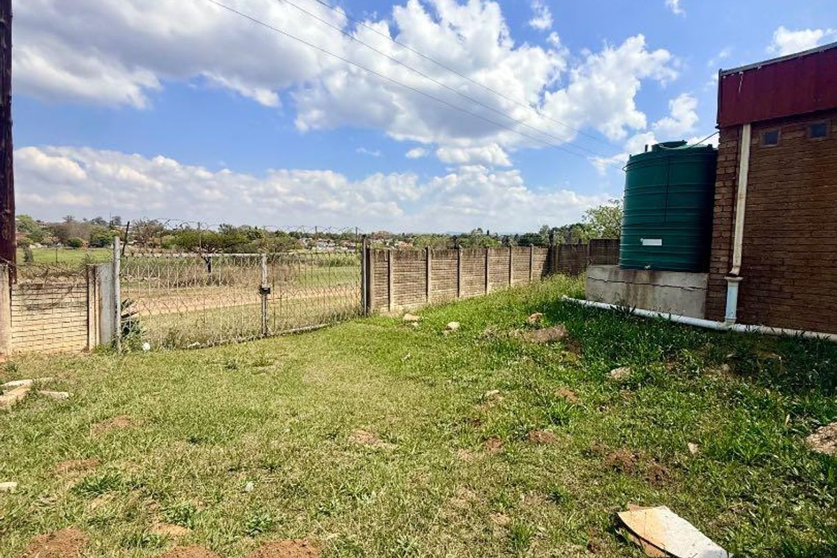 Rear exterior area featuring a brick boundary wall with razor wire fencing and a green water storage tank.