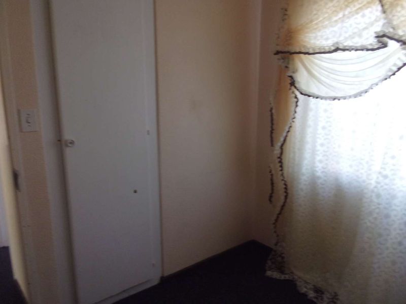 A small bedroom space featuring a built-in cupboard and a window with decorative curtains.