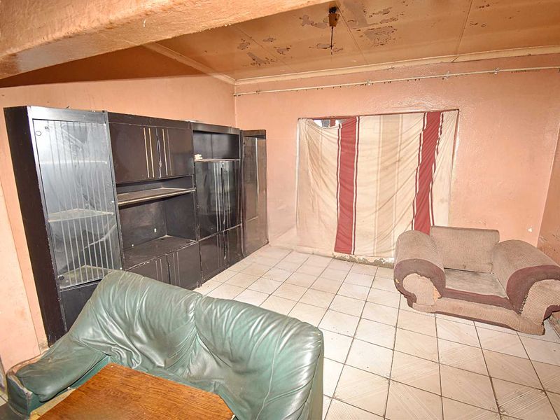 A living room space featuring tiled flooring and requiring significant cosmetic renovation to address wall and ceiling deterioration.