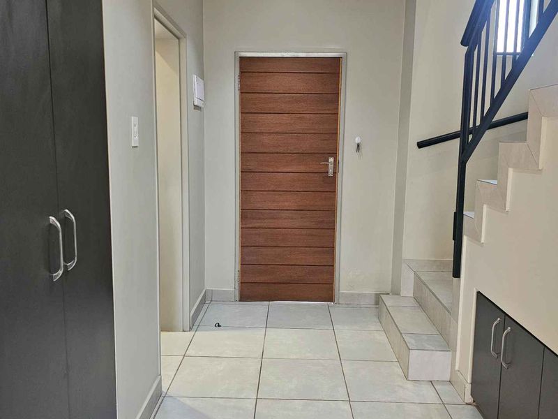 A clean and well-maintained entrance hall featuring tiled flooring, built-in storage cupboards, and a staircase with a modern metal railing.