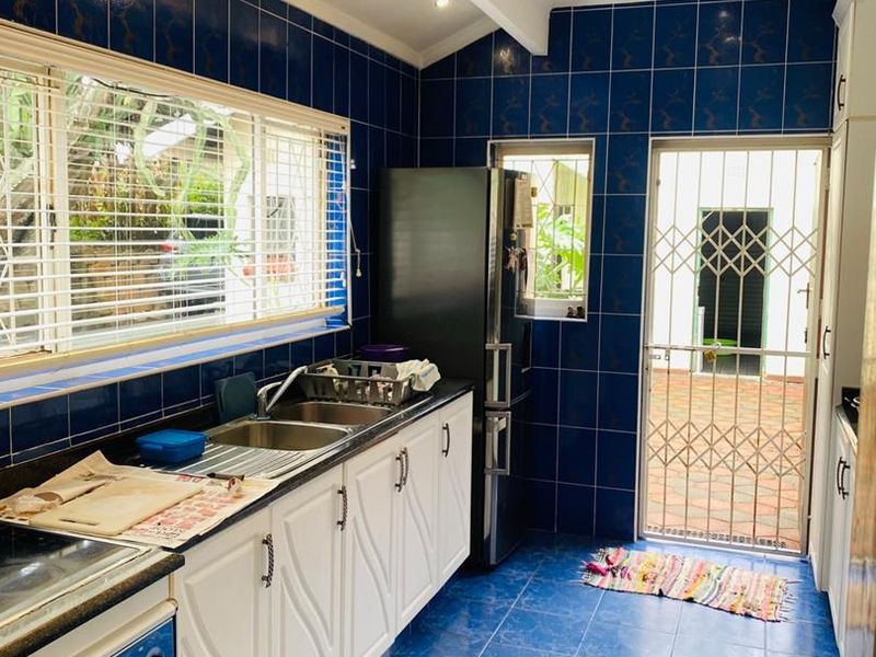 A functional kitchen featuring blue tiled walls and floors, white cabinetry, double sink, and direct access to an outdoor area via a security gate.