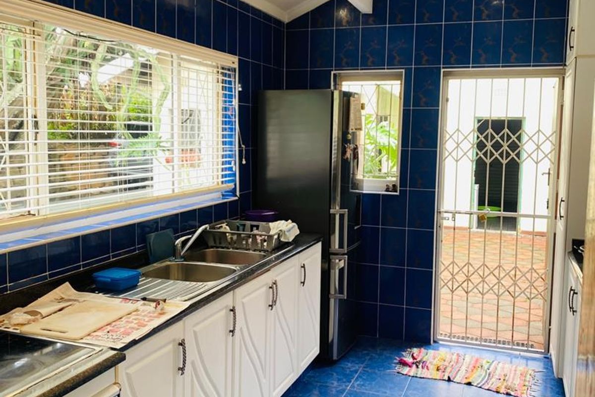 A functional kitchen featuring blue tiled walls and floors, white cabinetry, double sink, and direct access to an outdoor area via a security gate.