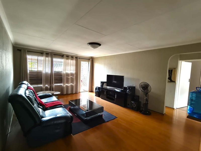 A spacious living room featuring laminate flooring, neutral wall tones, and an arched entryway leading to adjacent areas.