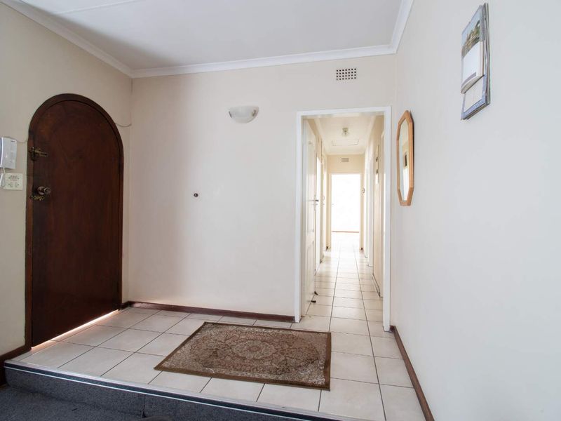 Entrance foyer featuring ceramic tiled flooring, an arched timber front door, and a direct hallway leading to the interior living spaces.
