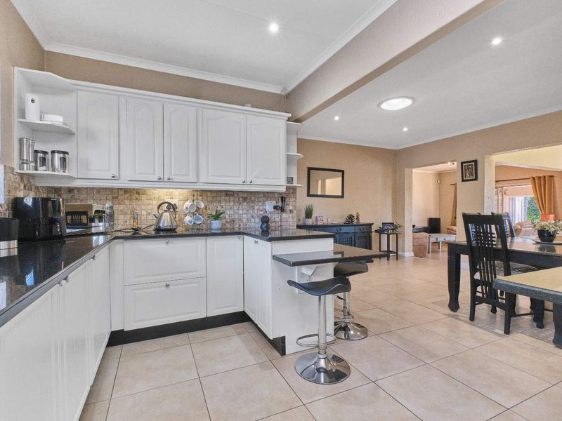 Open-plan kitchen featuring white cabinetry, black granite countertops, and a breakfast bar, seamlessly flowing into the adjacent dining and living areas.