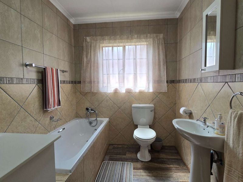 A functional bathroom featuring a bathtub, pedestal sink, and toilet with neutral wall tiling and wood-look flooring.