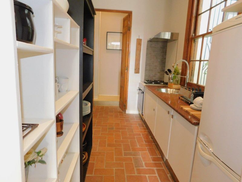 A compact galley-style kitchen featuring terracotta flooring, stone countertops, built-in cabinetry, and a gas hob with an extractor fan.