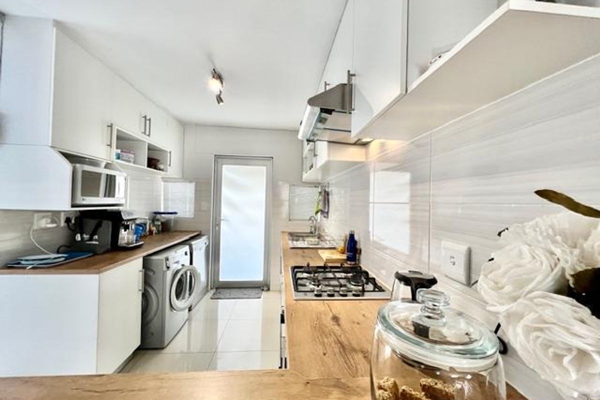 Modern galley-style kitchen featuring white cabinetry, wood-look countertops, gas hob, extractor fan, and integrated laundry appliances with direct access to the exterior.