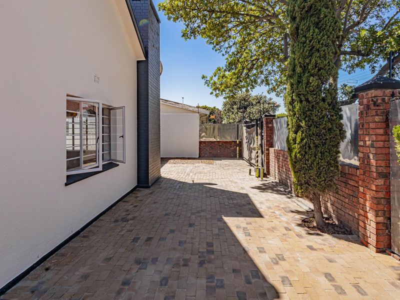 A well-maintained paved side yard or rear exterior area featuring brick boundary walls and secure casement windows.