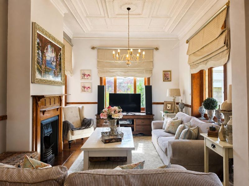 A charming living room featuring a classic fireplace with a timber mantelpiece, intricate coffered ceilings, and warm hardwood flooring.