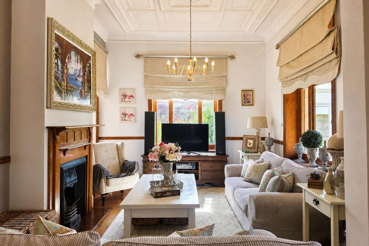 A charming living room featuring a classic fireplace with a timber mantelpiece, intricate coffered ceilings, and warm hardwood flooring.