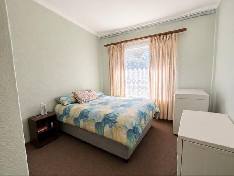 A standard bedroom featuring neutral wall paint, carpet flooring, and a window with fitted curtain rods.