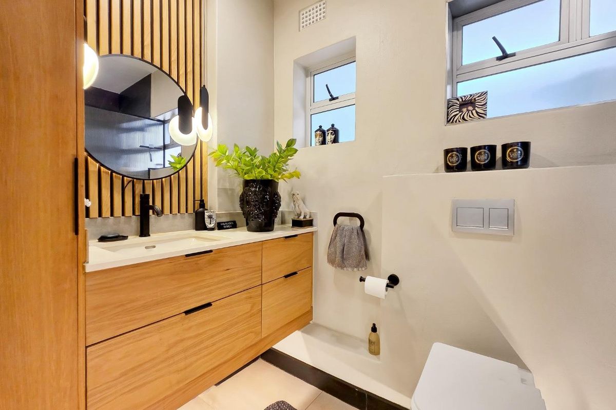 Modern bathroom featuring a timber vanity with integrated basin, slatted wood feature wall, and a concealed cistern toilet with dual flush plate.