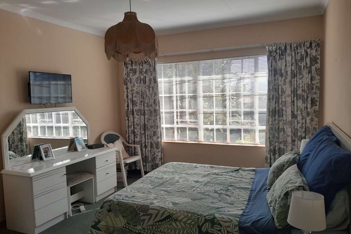 A bedroom featuring large windows with blinds, carpeted flooring, and a ceiling-mounted light fixture.