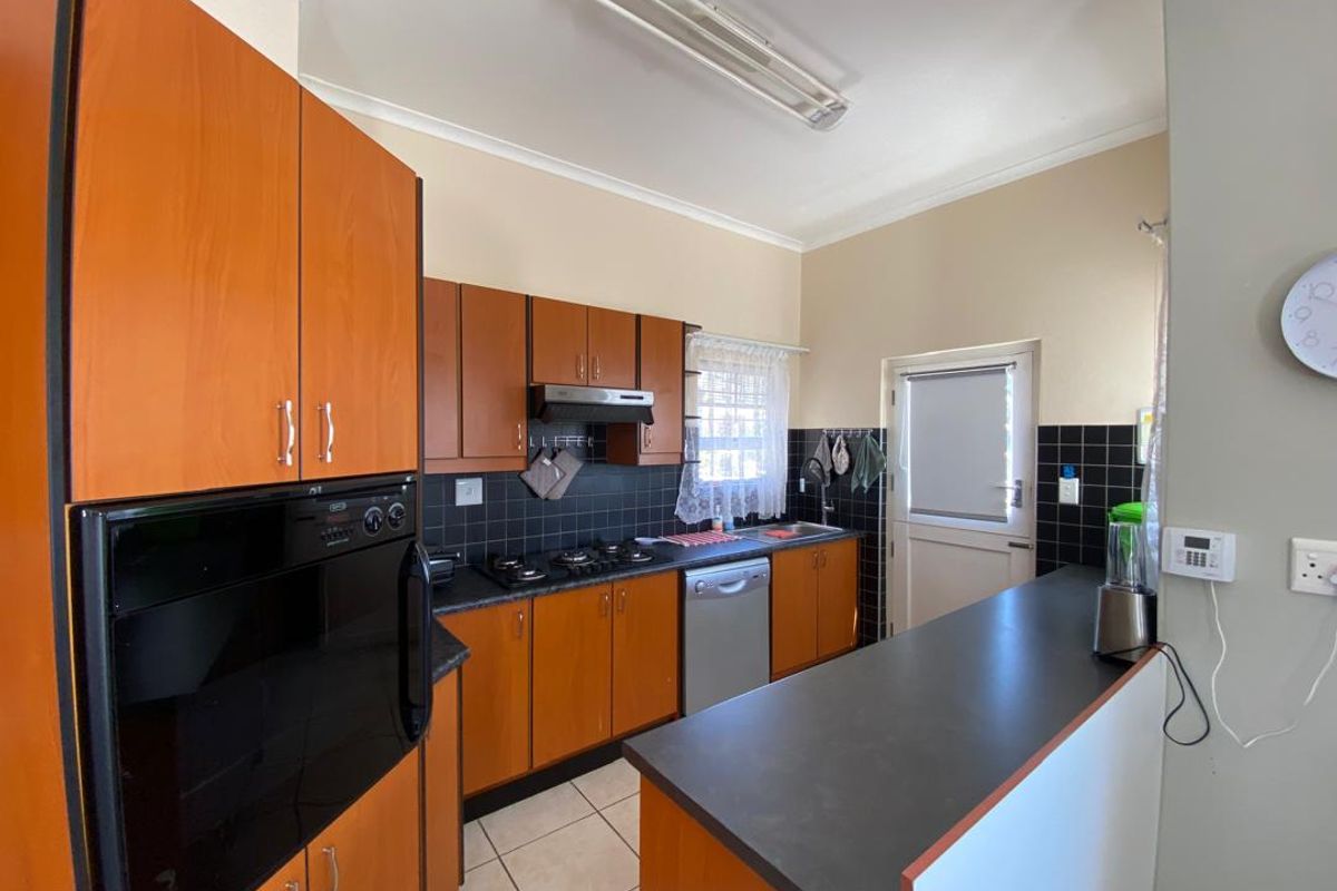 A functional kitchen featuring wood-finish cabinetry, black tiled splashbacks, a built-in oven, gas hob, and a breakfast bar counter.