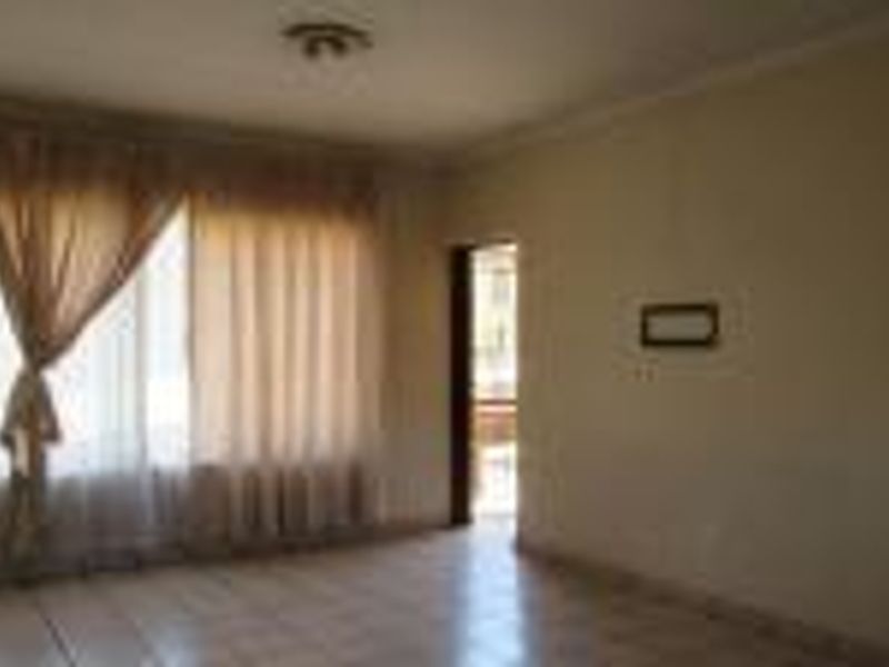 An empty living room featuring tiled flooring, ceiling cornice, and natural light through a large window.