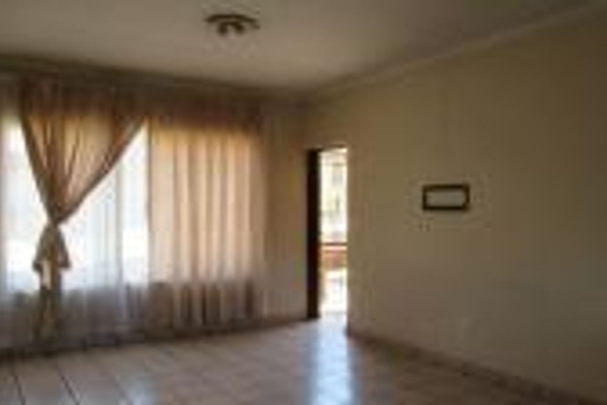 An empty living room featuring tiled flooring, ceiling cornice, and natural light through a large window.