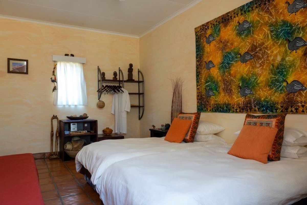 A bedroom featuring terracotta floor tiles, textured wall finishes, and a window with natural light.