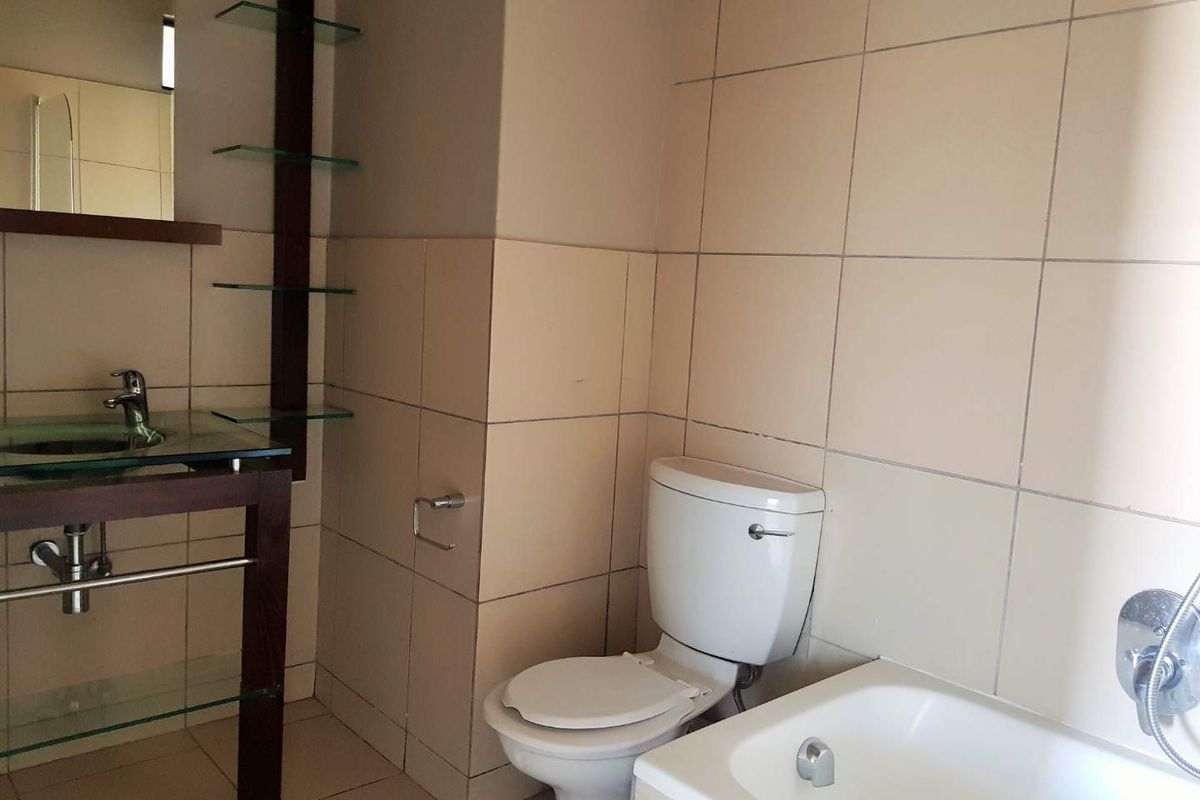A functional bathroom featuring a glass vessel sink, wall-mounted shelving, a standard toilet, and a bathtub with integrated shower fixtures.