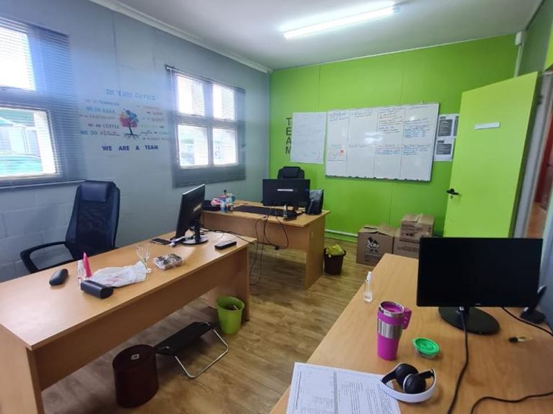 A functional office space featuring laminate flooring, large windows for natural light, and a wall-mounted whiteboard, suitable for a collaborative work environment.